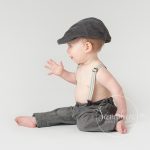 Cute baby boy sitting up wearing a flat cap in Sussex