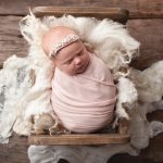 baby girl swaddled in pink in a wooden bed showing baby portraits billinghurst by samphire photography