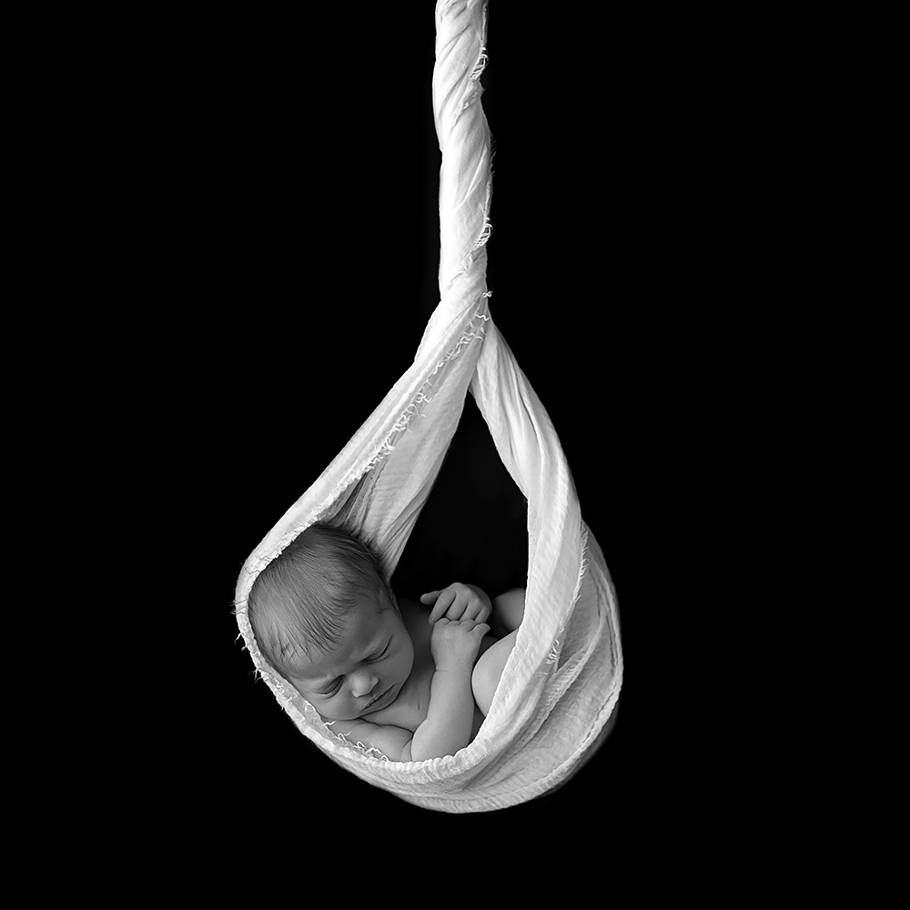 Black and white composite of newborn baby cradled in fabric
