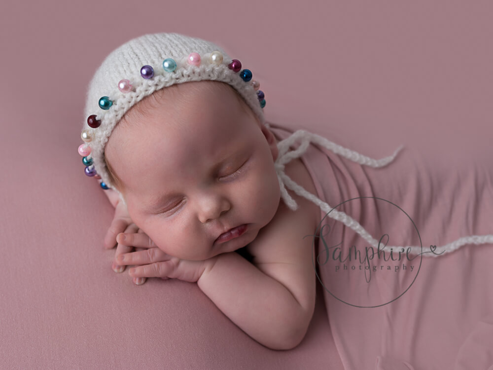 sleeping babay girl with head on hands wearing rainbow beaded hat