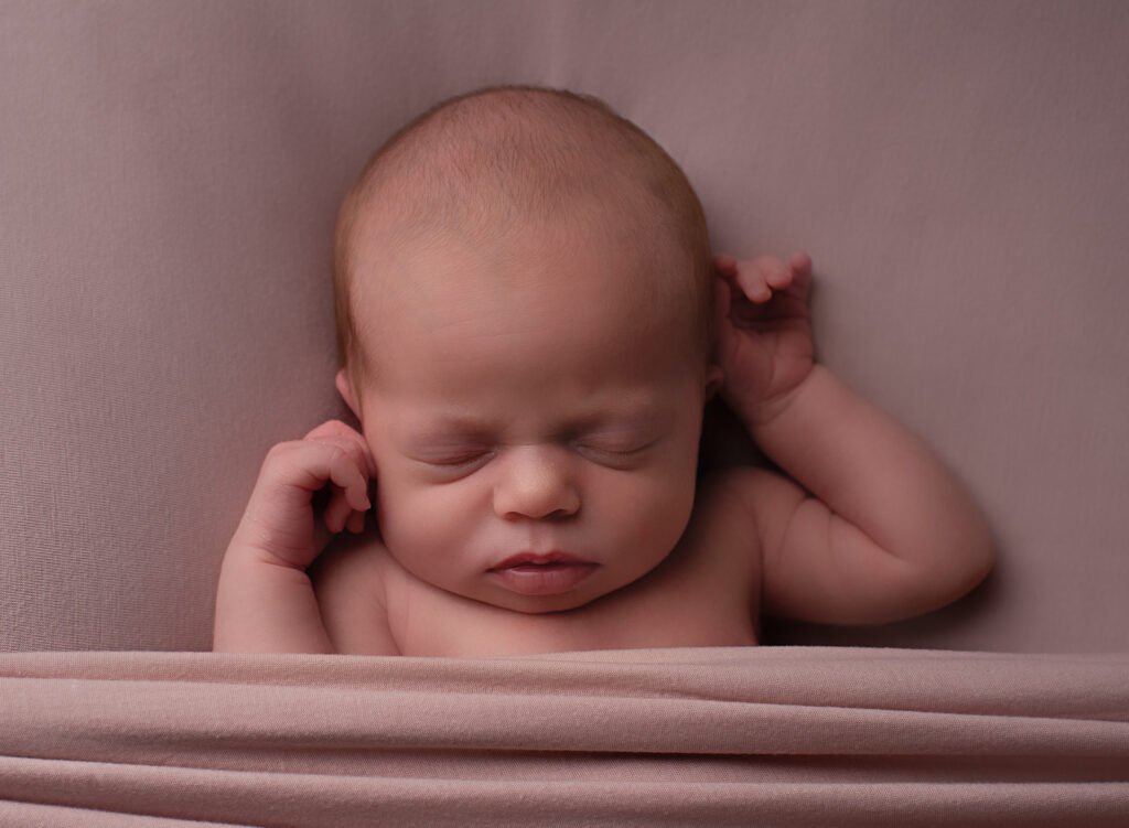 Newborn baby girl asleep on pink fabric