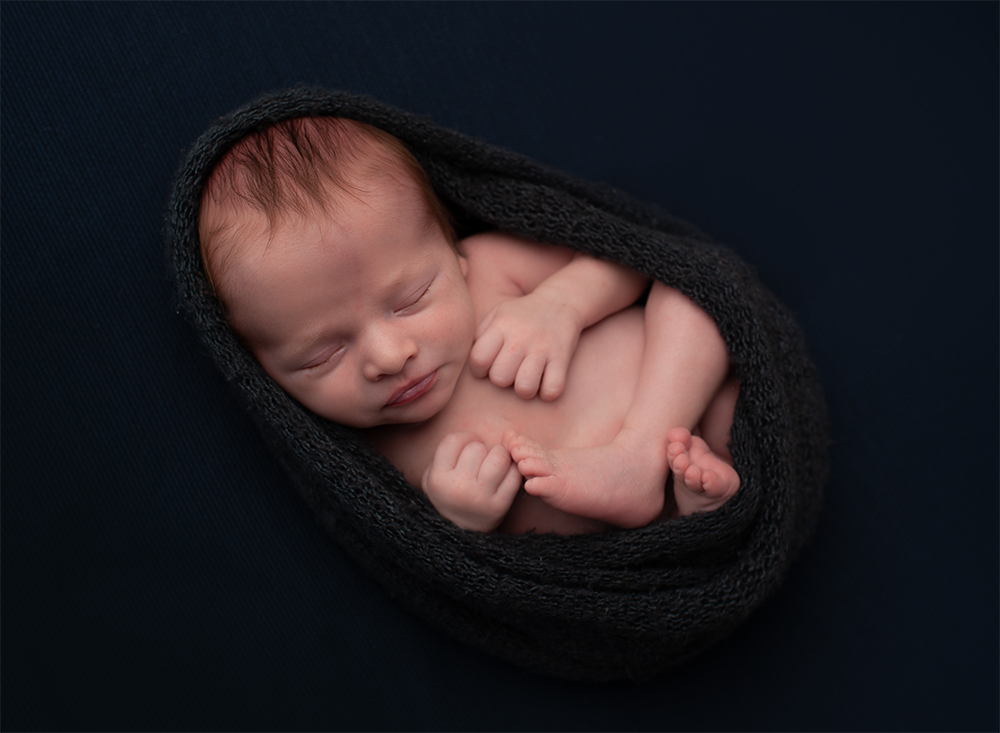 Newborn baby boy posed in egg wrap
